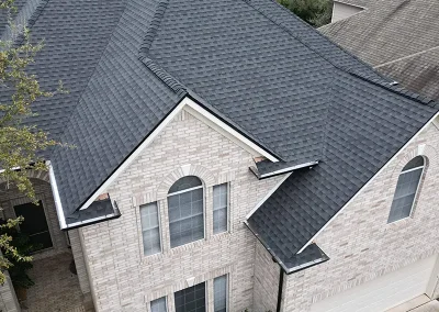 inf-02 - Infinity Roofing - A Stronghouse Partner A two-story brick house with a steep gray shingled roof and multiple gables, seen from an elevated angle.