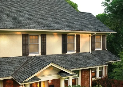 inf-06 - Infinity Roofing - A Stronghouse Partner Two-story house with a slate roof, beige upper level, brick lower level, white columns, and a small covered front porch.