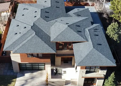 inf-08 - Infinity Roofing - A Stronghouse Partner Aerial view of a modern, multi-level house with layered gray shingle roofs and a two-car garage on the left.