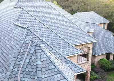 inf-09 - Infinity Roofing - A Stronghouse Partner Aerial view of brick houses with blue-gray slate tile roofs. There are multiple gabled sections and green landscaping nearby.